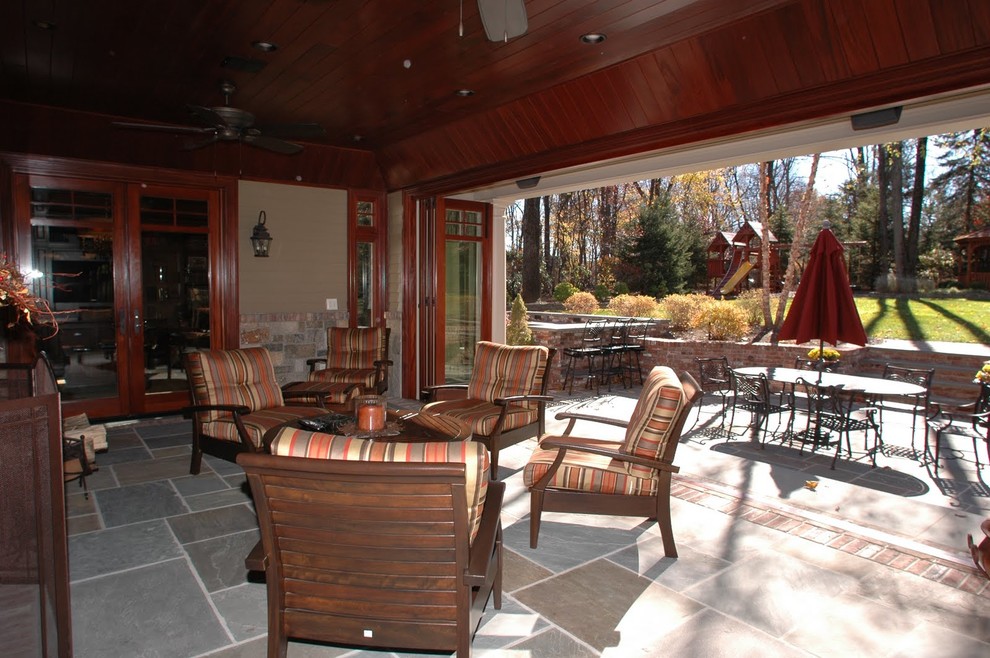 Réalisation d'une terrasse arrière tradition de taille moyenne avec un foyer extérieur, des pavés en pierre naturelle et une extension de toiture.