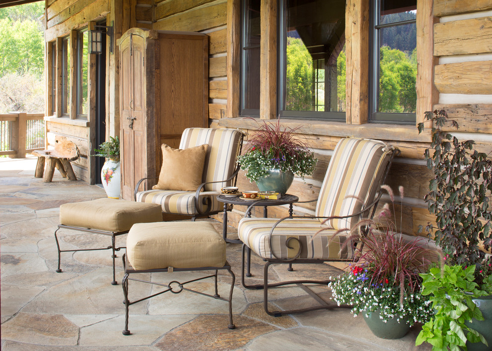 This is an example of a rustic stone porch design in Denver with a roof extension.