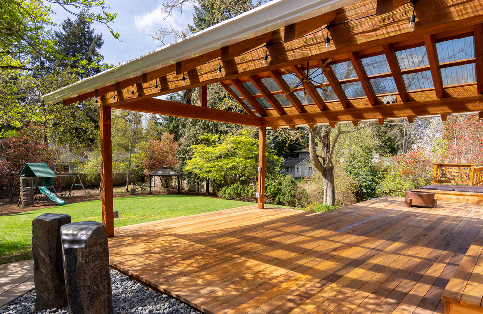 Exemple d'un très grand porche d'entrée de maison arrière tendance avec un foyer extérieur, une terrasse en bois, une extension de toiture et un garde-corps en bois.