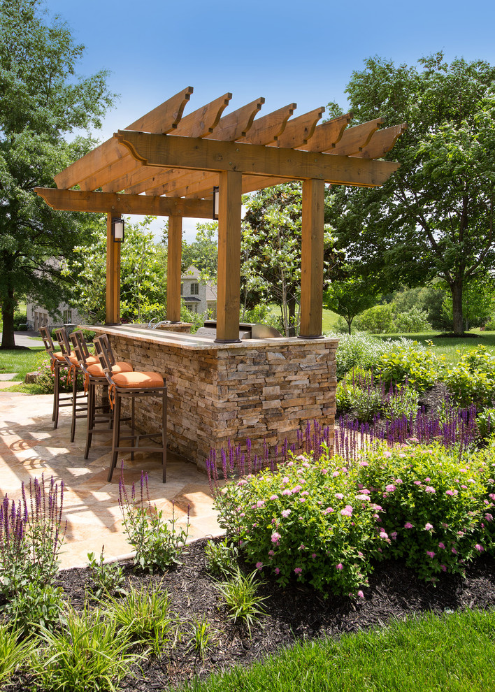 Ejemplo de terraza clásica renovada en patio trasero con adoquines de piedra natural, pérgola y cocina exterior
