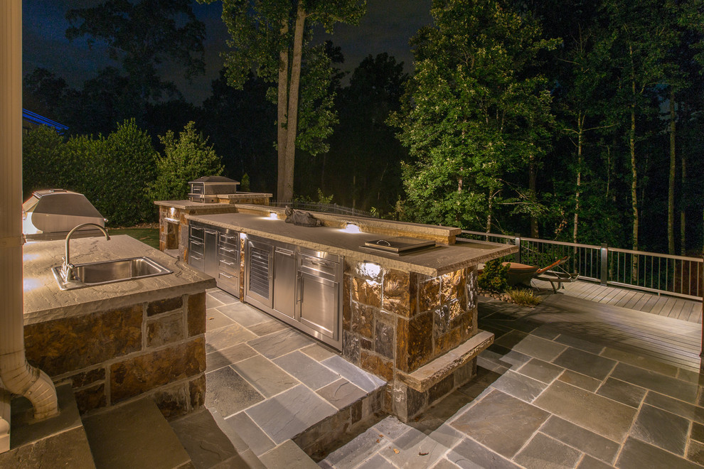 This is an example of a large traditional back veranda in Charlotte with an outdoor kitchen and natural stone paving.