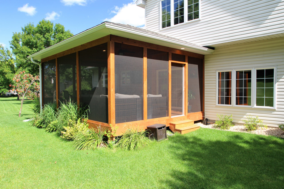 Cette image montre un grand porche d'entrée de maison arrière chalet avec une moustiquaire, une terrasse en bois et une extension de toiture.