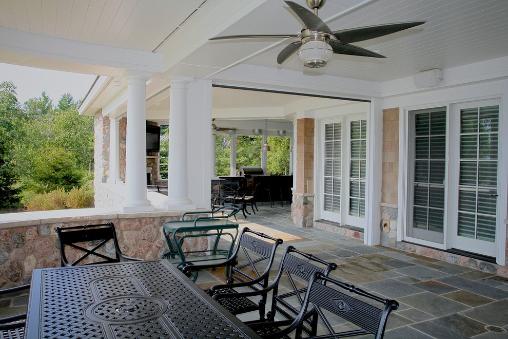 Exemple d'un grand porche d'entrée de maison arrière chic avec une cuisine d'été, des pavés en pierre naturelle et une extension de toiture.