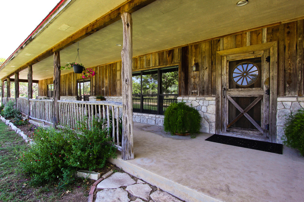 Bild på en stor rustik veranda framför huset, med takförlängning, en öppen spis och betongplatta
