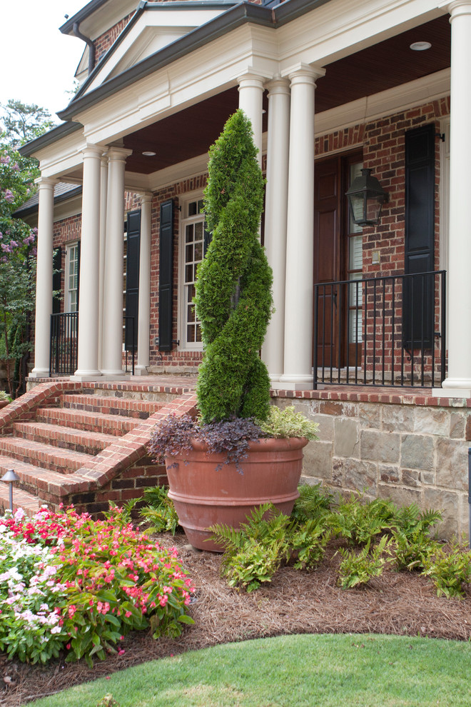 This is an example of a large traditional brick front porch design in Atlanta with a roof extension.
