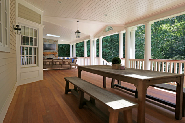 Cette image montre un grand porche d'entrée de maison arrière traditionnel avec un foyer extérieur, une terrasse en bois et une extension de toiture.