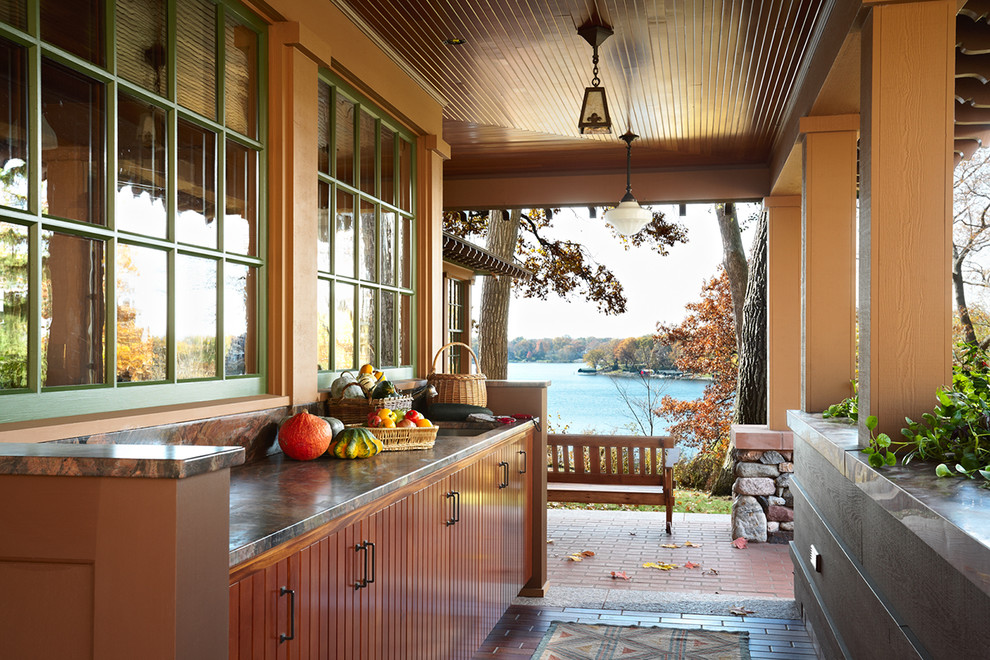 Inspiration för stora amerikanska verandor längs med huset, med takförlängning och marksten i tegel