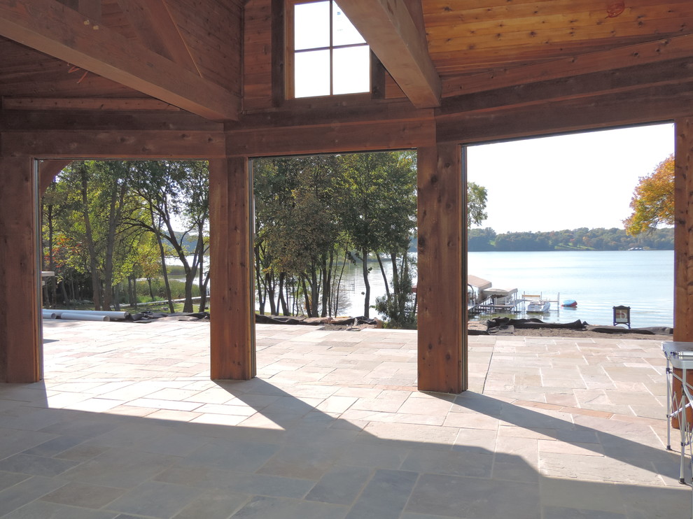 This is an example of an expansive rustic back screened veranda in Minneapolis with a roof extension and natural stone paving.