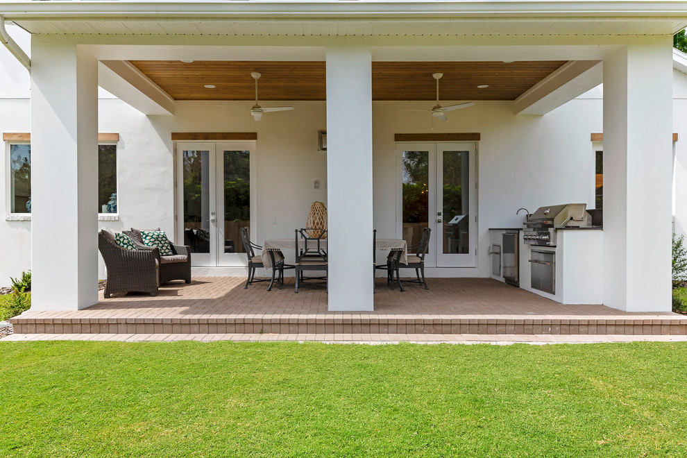 Cette image montre un grand porche d'entrée de maison arrière avec une cuisine d'été, des pavés en brique et une extension de toiture.