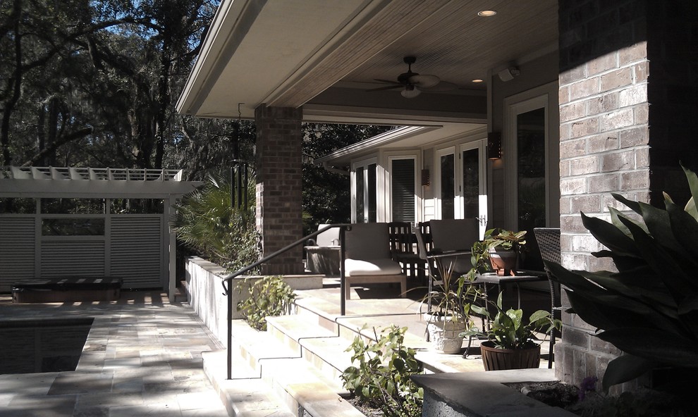This is an example of a coastal stone back porch design in Charleston with a roof extension.