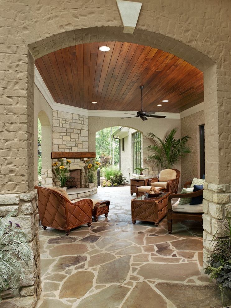 Cette photo montre un grand porche d'entrée de maison arrière chic avec un foyer extérieur, des pavés en pierre naturelle et une extension de toiture.