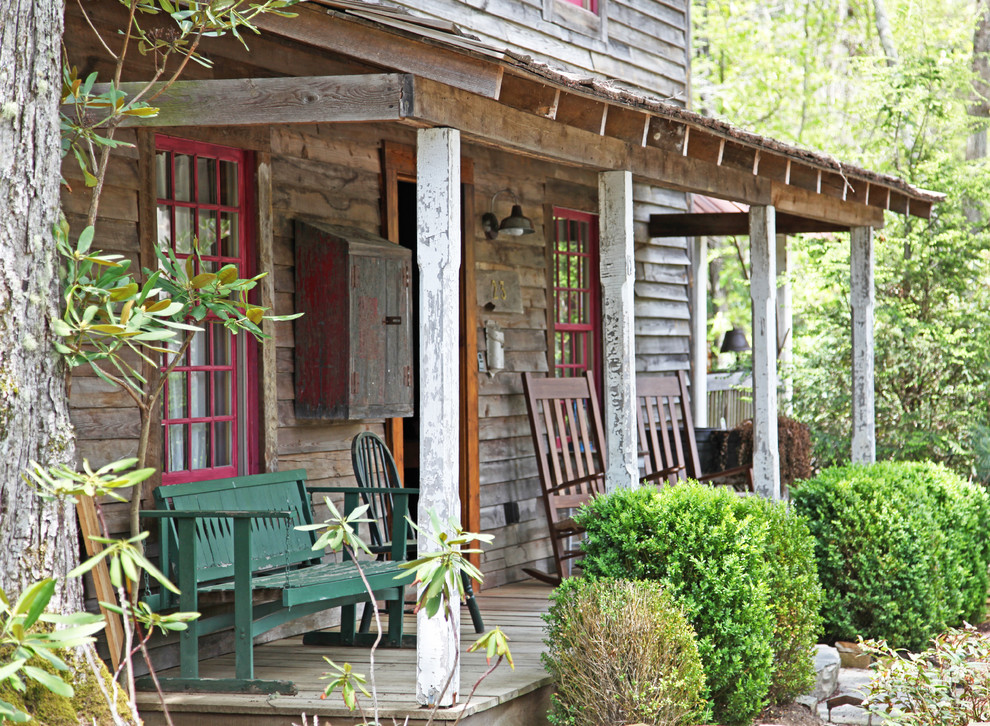 Bild på en liten rustik veranda framför huset, med trädäck och takförlängning
