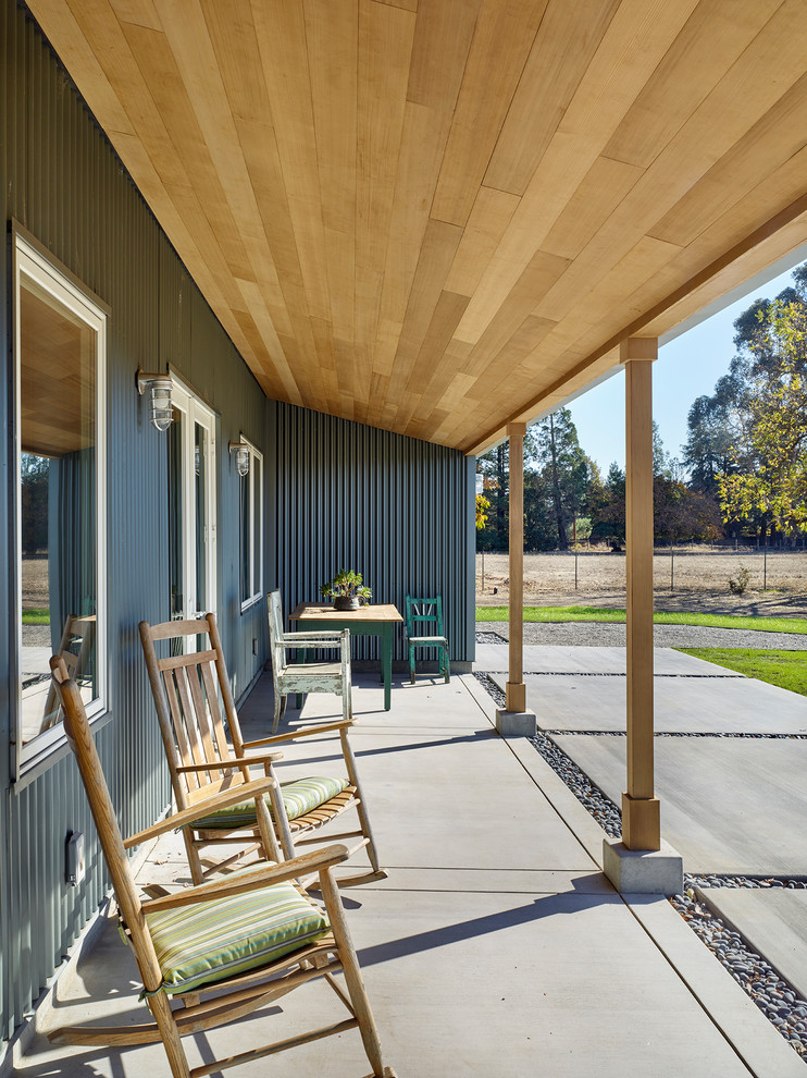 Foto på en lantlig veranda, med betongplatta och takförlängning