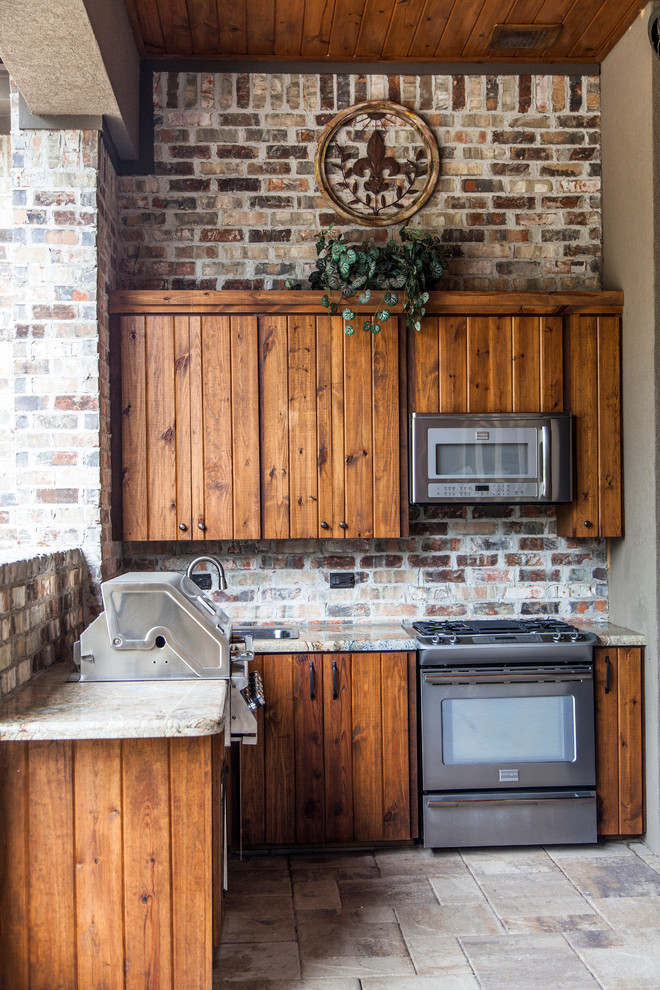 Überdachte Veranda hinter dem Haus mit Outdoor-Küche und Natursteinplatten in Houston