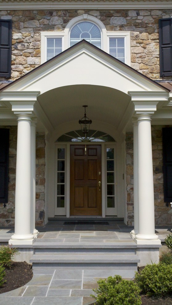 This is an example of a large rural front veranda in Philadelphia with natural stone paving and a roof extension.