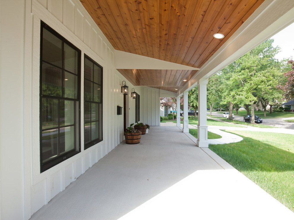 Cette image montre un grand porche d'entrée de maison avant rustique avec une extension de toiture, des colonnes et une dalle de béton.