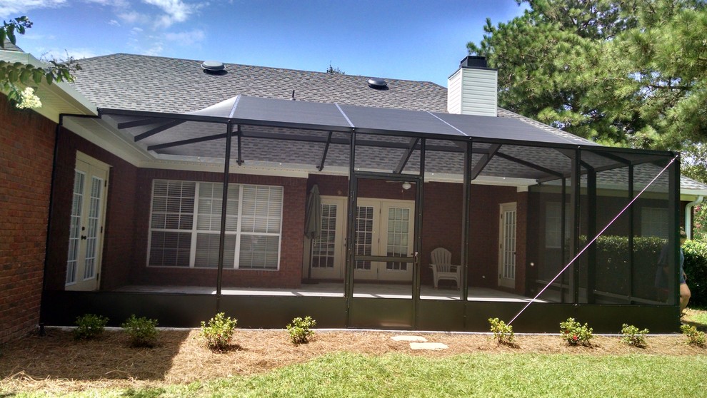Large classic concrete screened-in back porch idea in Miami with a roof extension