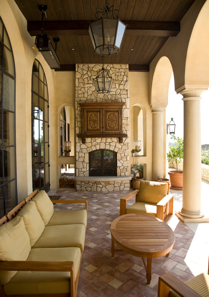 Large mediterranean back veranda in Los Angeles with a fireplace, a roof extension and brick paving.