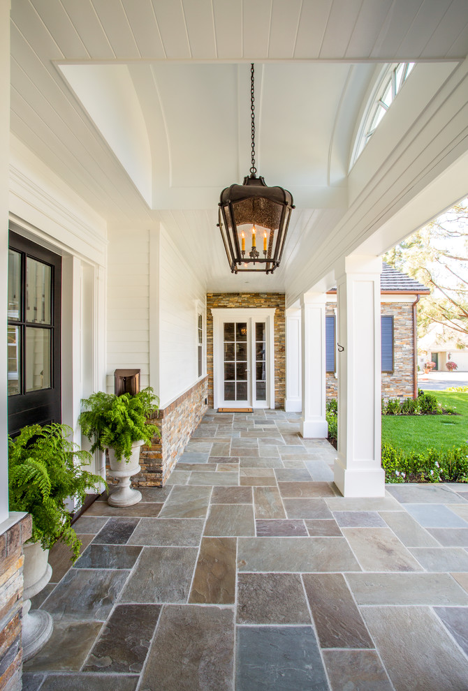 This is an example of a medium sized traditional front veranda in Orange County with a roof extension, natural stone paving and feature lighting.