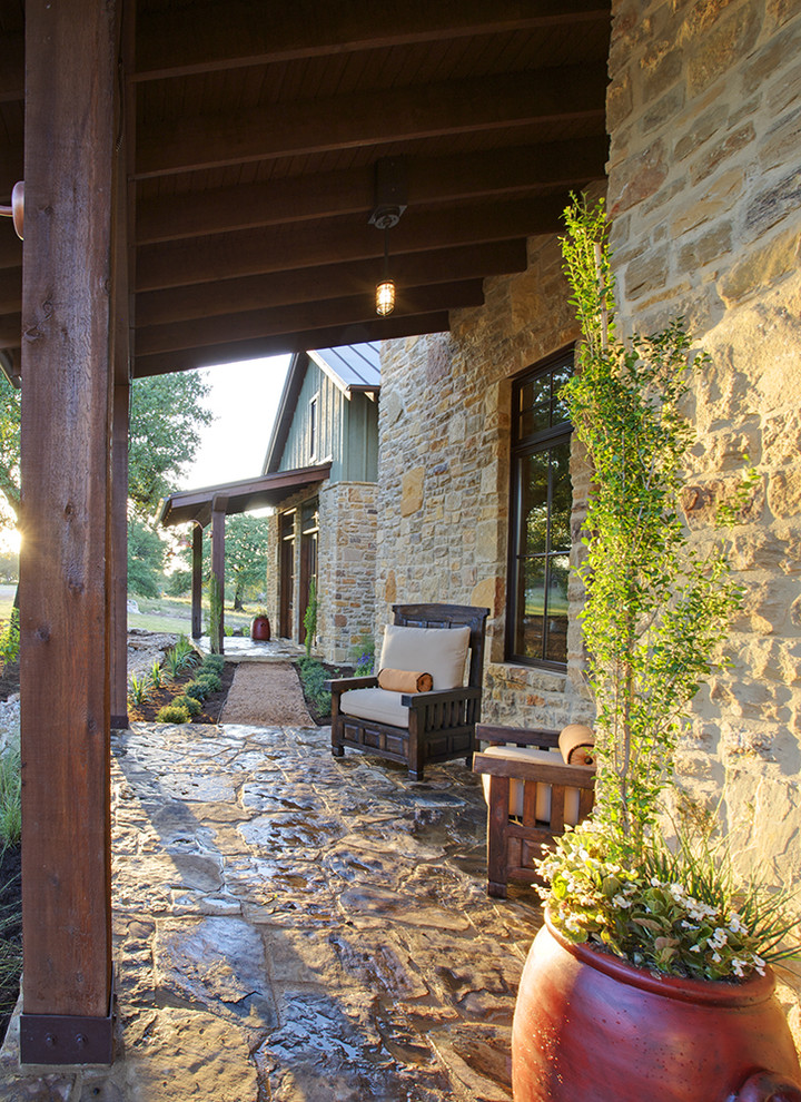 This is an example of a farmhouse stone porch design in Austin with a roof extension.