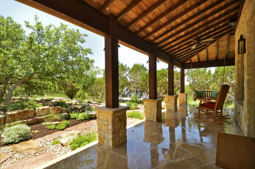 This is an example of a rustic stone porch design in Austin with a roof extension.