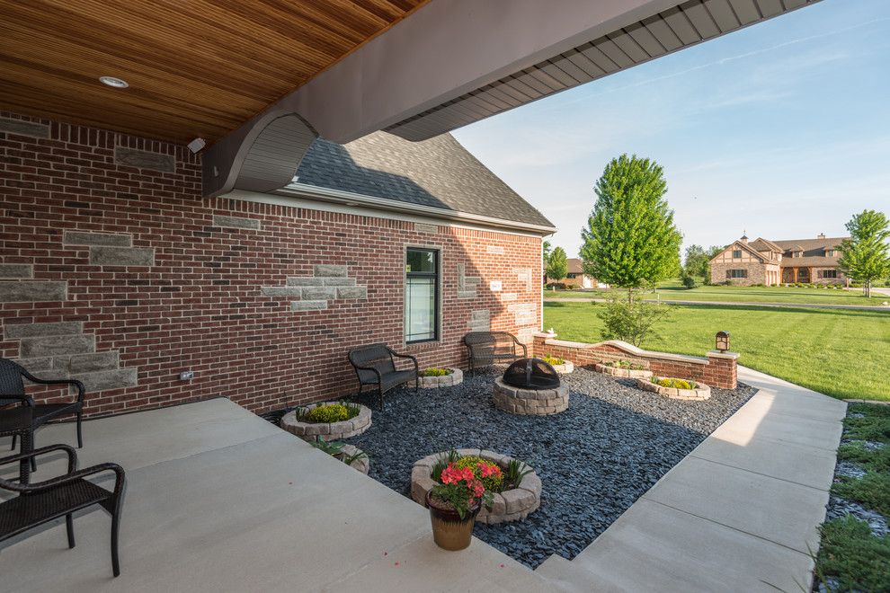 Cette photo montre un grand porche d'entrée de maison avant tendance avec un foyer extérieur, une dalle de béton et une extension de toiture.