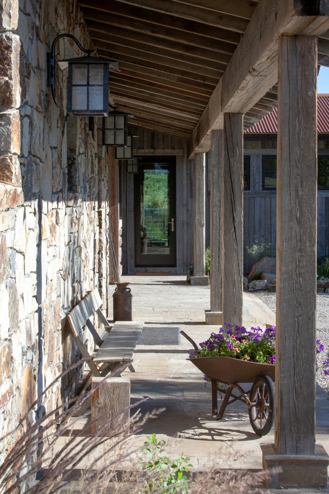 Foto på en mellanstor rustik veranda framför huset, med naturstensplattor och takförlängning