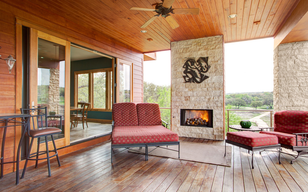 Cette image montre un porche d'entrée de maison arrière design avec une cheminée, une terrasse en bois, une extension de toiture et un garde-corps en matériaux mixtes.