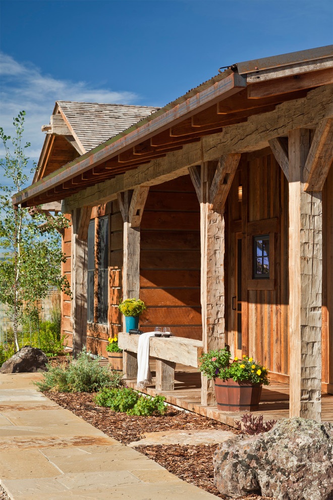 Foto på en rustik veranda framför huset, med utekrukor, takförlängning och naturstensplattor