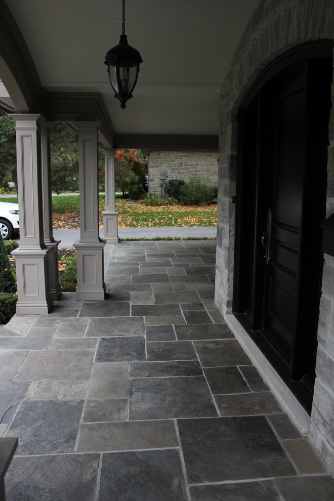 Immagine di un grande portico tradizionale davanti casa con un portico chiuso e pavimentazioni in pietra naturale