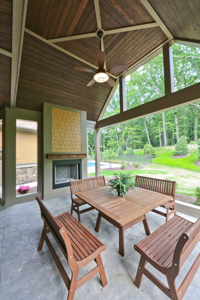 Idée de décoration pour un grand porche d'entrée de maison arrière tradition avec un foyer extérieur, une dalle de béton et une extension de toiture.