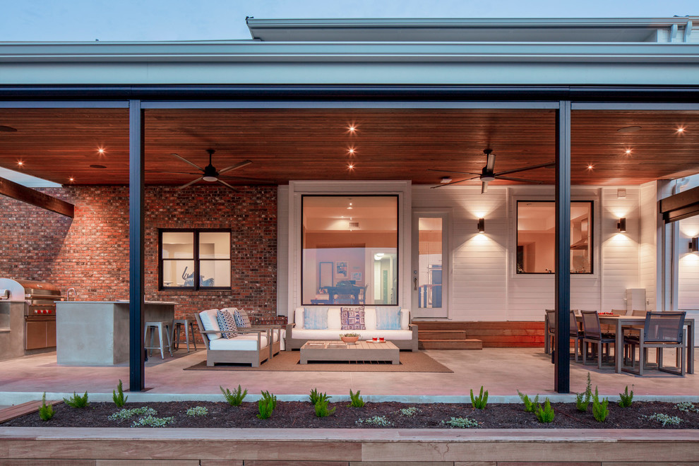 Diseño de terraza actual grande en patio trasero con cocina exterior, losas de hormigón y toldo