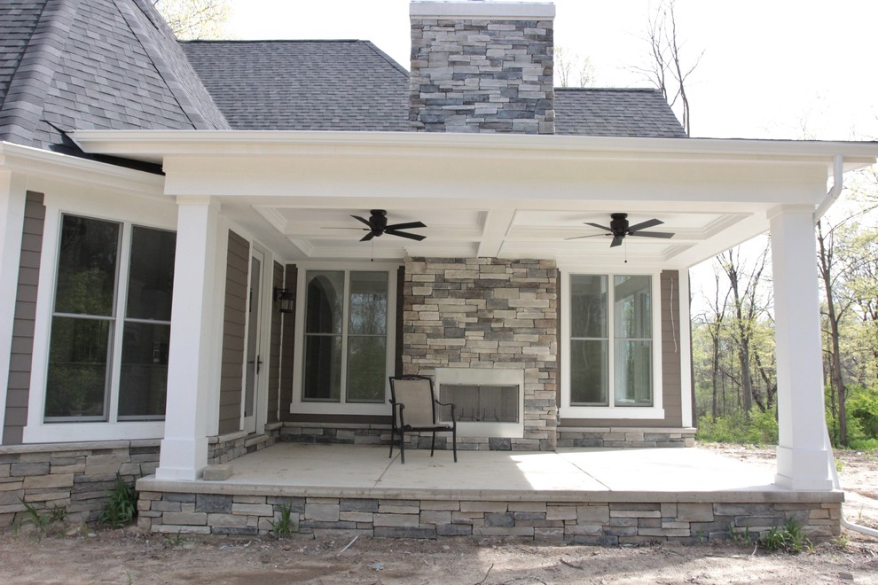 Idéer för att renovera en mellanstor amerikansk veranda på baksidan av huset, med en öppen spis, betongplatta och takförlängning