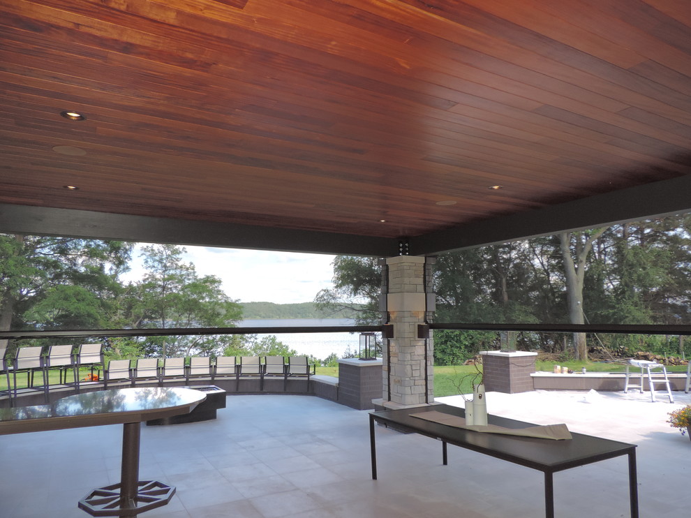 Réalisation d'un grand porche d'entrée de maison arrière design avec une moustiquaire, une extension de toiture et des pavés en béton.