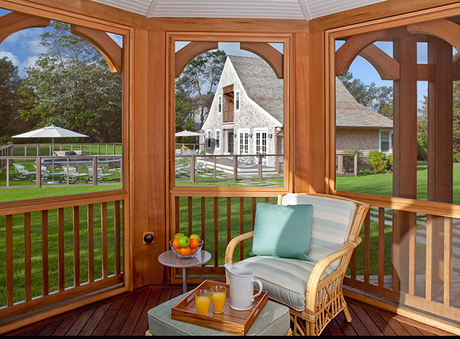 Idée de décoration pour un grand porche d'entrée de maison avant champêtre avec une moustiquaire, une terrasse en bois et une extension de toiture.