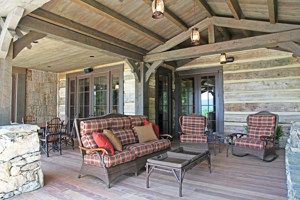 Idée de décoration pour un grand porche d'entrée de maison arrière chalet avec un foyer extérieur, une terrasse en bois et une extension de toiture.