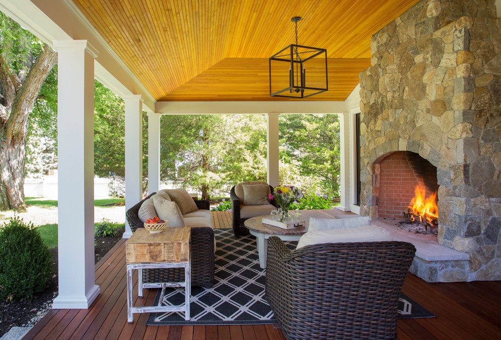 Cette image montre un grand porche d'entrée de maison arrière rustique avec un foyer extérieur, une extension de toiture et une terrasse en bois.