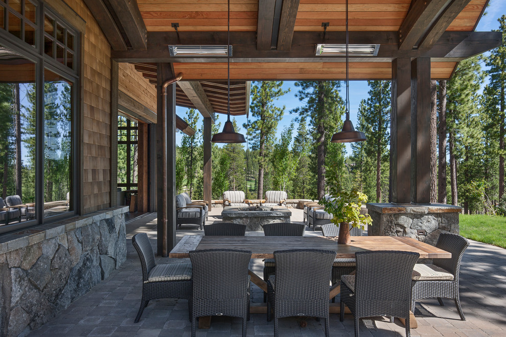 Aménagement d'un grand porche d'entrée de maison arrière avec un foyer extérieur, des pavés en pierre naturelle et une extension de toiture.