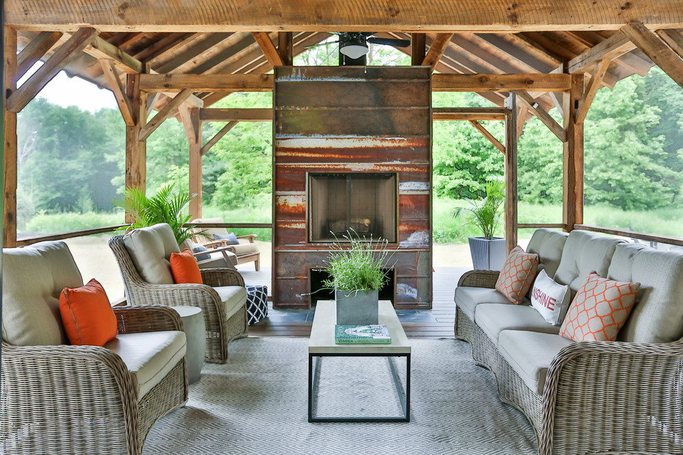 Réalisation d'un porche d'entrée de maison arrière champêtre avec un foyer extérieur, une terrasse en bois et une extension de toiture.