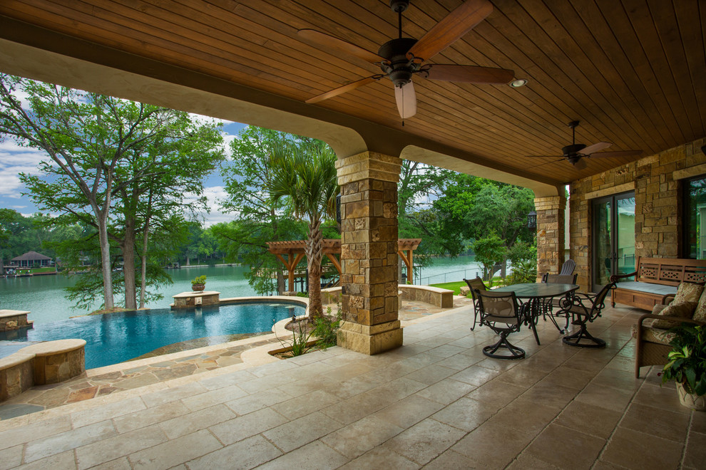 This is an example of a large mediterranean stone back porch design in Austin with a roof extension.