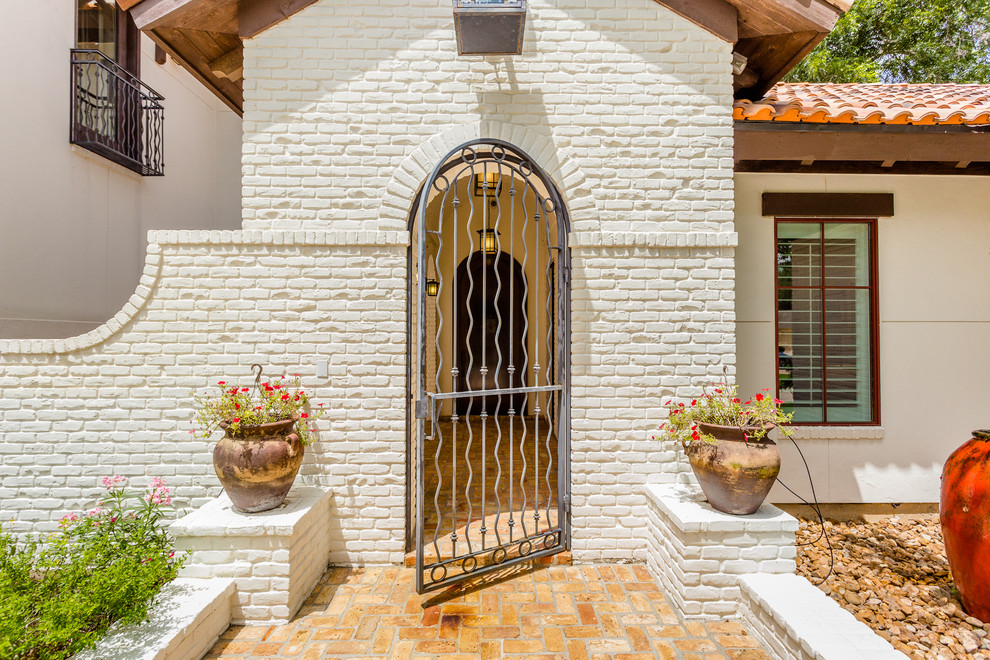 Cette photo montre un grand porche d'entrée de maison avant méditerranéen avec un point d'eau, des pavés en brique et un auvent.