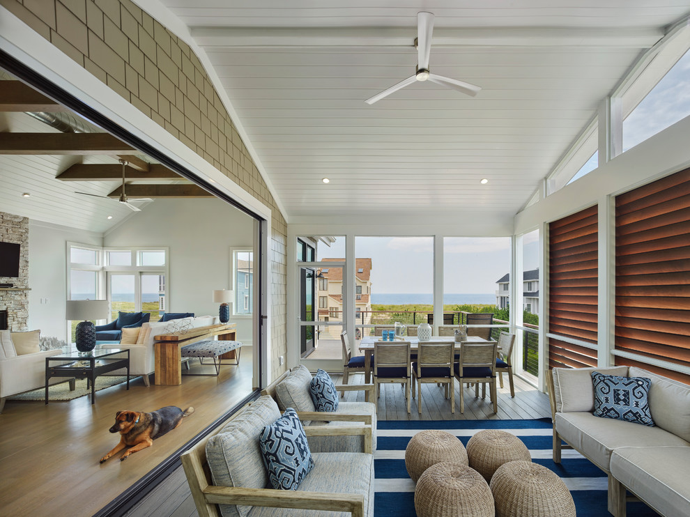 Cette photo montre un grand porche d'entrée de maison bord de mer avec une extension de toiture, une moustiquaire et une terrasse en bois.