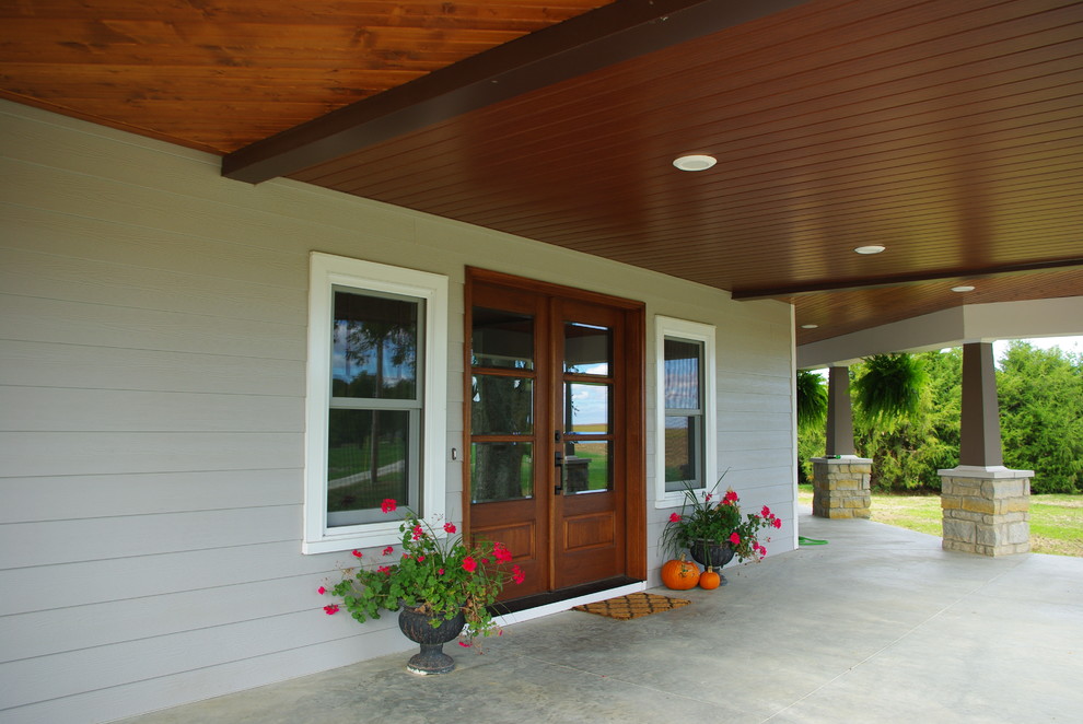 This is an example of a large country front veranda in St Louis with a roof extension and concrete paving.