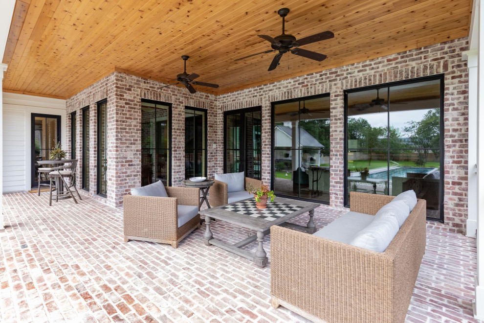Idée de décoration pour un grand porche d'entrée de maison arrière champêtre avec des pavés en brique et une extension de toiture.