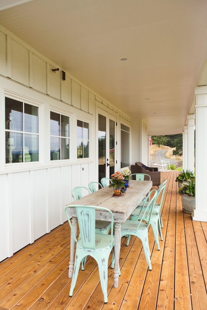 Foto på en stor lantlig veranda framför huset, med trädäck och takförlängning