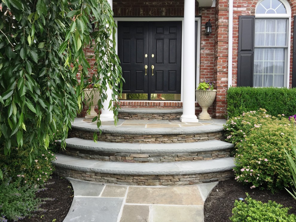 This is an example of a mid-sized traditional stone front porch design in New York.