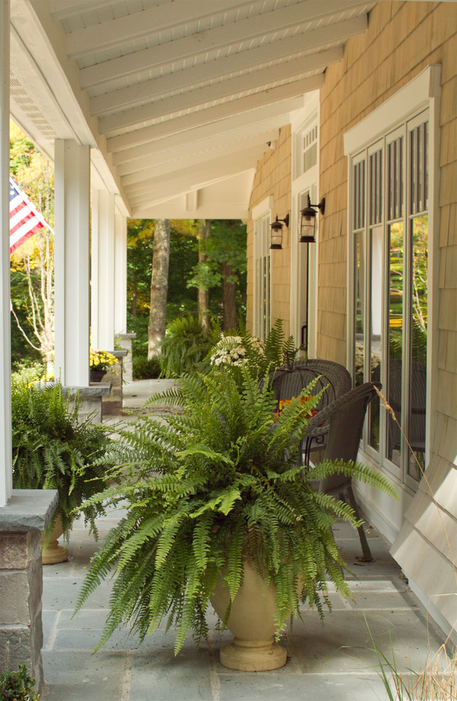 Inspiration för en stor amerikansk veranda framför huset, med naturstensplattor, takförlängning och utekrukor