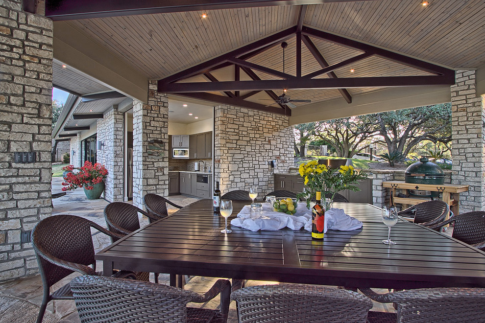 This is an example of a large contemporary side veranda in Austin with an outdoor kitchen, natural stone paving and a roof extension.