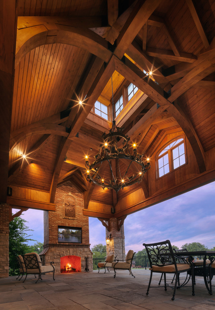 Idée de décoration pour un très grand porche d'entrée de maison arrière chalet avec un foyer extérieur, une extension de toiture et des pavés en pierre naturelle.