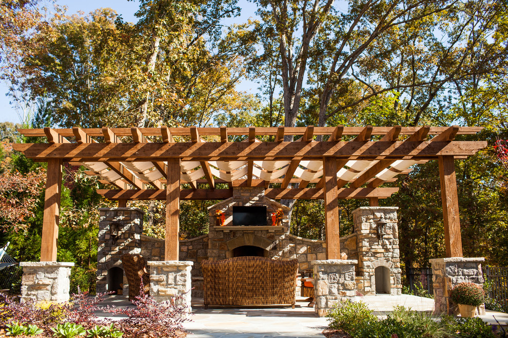 Diseño de terraza tradicional grande en patio trasero con adoquines de piedra natural, pérgola y chimenea